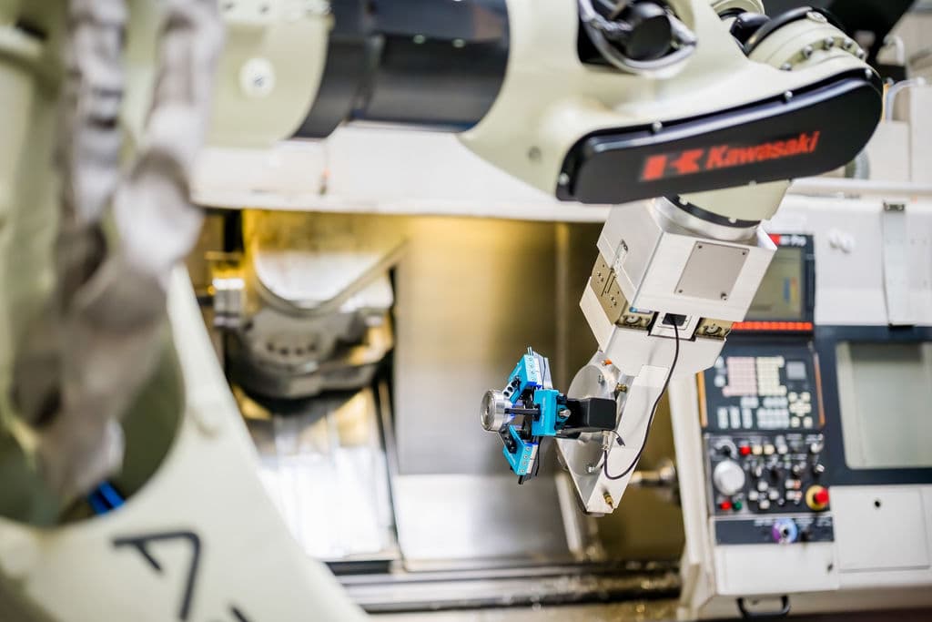 A Kawasaki robot carrying a machined part — payload spent on the part, not the gripper
